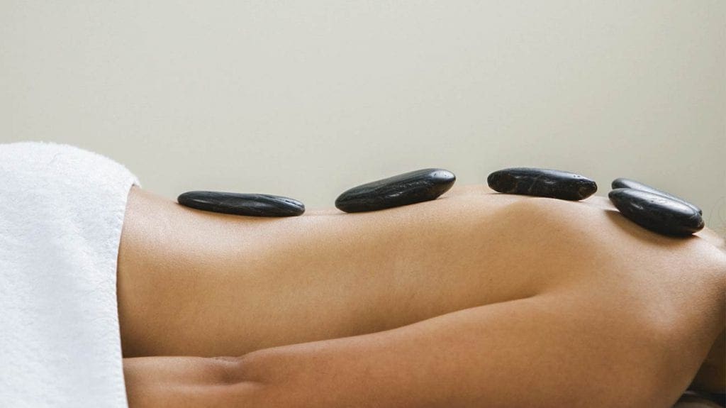 Hot stones on a woman's back as she lays on a massage table.